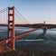 Golden Gate Bridge extending over water with boats below, against a backdrop of hills and a clear sky.