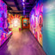 A colorful exhibit hallway with vibrant murals, text panels, and display cases, illuminated by purple lighting.