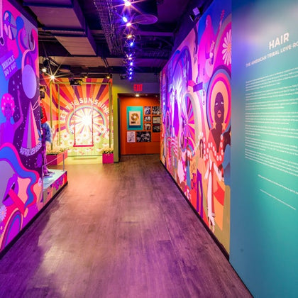 A colorful exhibit hallway with vibrant murals, text panels, and display cases, illuminated by purple lighting.