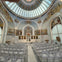 A church interior with a domed ceiling, religious murals, white chairs, and an ornate altar at the front.