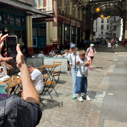 Two people posing for a photo while another person takes their picture in a lively outdoor market setting with tables and chairs.