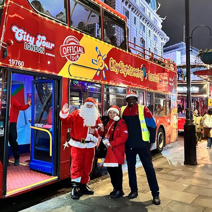 Three people stand in front of a red City Sightseeing double-decker bus, two dressed in Santa outfits and one in a safety vest.
