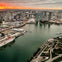 Aerial view of a cityscape at sunset with high-rise buildings, a bridge, a docked cruise ship, and a waterfront area.