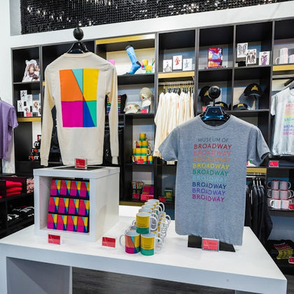 A retail display featuring colorful Broadway-themed merchandise, including shirts, mugs, and other items on shelves.