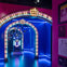 A brightly-lit, colorful archway leading to a display of objects under blue lighting, with framed pictures on the wall.
