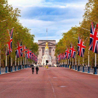 A wide street lined with British flags and trees, leading to a monument and a large historic building in the background.