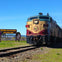 A train approaches on a railway next to a sign that reads, "Welcome to this world-famous wine-growing region, Napa Valley."