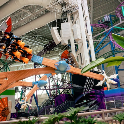 An indoor amusement park with a ride featuring orange seats and a wooden arm, surrounded by colorful structures.