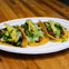 Three tacos on a white plate, topped with meat, cilantro, onions, and pineapple slices, placed on a wooden table.