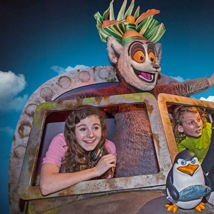 Two children and a character in a large animal costume look out of an airplane window with a penguin figure in the foreground.