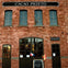 A brick building with arched windows and doors, the sign "Cacao Prieto" above. Two small flags and a chalkboard are outside.