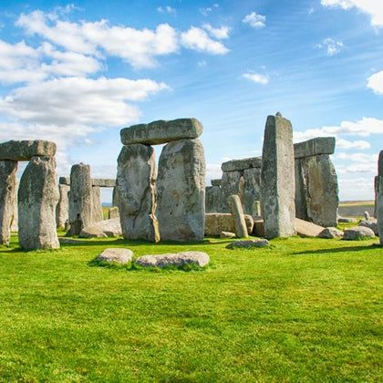 Stonehenge, a prehistoric monument, featuring large standing stones on a grassy field under a partly cloudy sky.