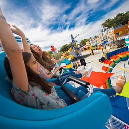 People enjoying a ride at an amusement park with colorful structures and a bright, vibrant atmosphere.