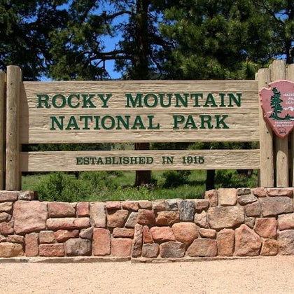 Sign for Rocky Mountain National Park, established in 1915, made of wood and stone, with trees in the background.