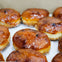 Glazed apple fritters arranged in rows on a white paper-lined surface.
