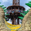 People ride a drop tower amusement ride, surrounded by large, decorative green spikes and stone structures under a blue sky.