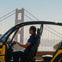 A person in a small enclosed vehicle with the Golden Gate Bridge visible in the background on a sunny day.
