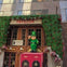 A building entrance decorated with green foliage, flowers, and a cheerful leprechaun figure, with the sign 'PAPILLON' above.