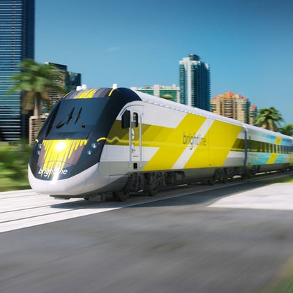 A sleek yellow and white train traveling through a cityscape with modern buildings and palm trees under a clear sky.