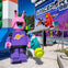 A Lego alien figure in purple stands outdoors near a space-themed display, with a Lego astronaut in red in the background.