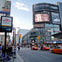 A busy urban intersection with pedestrians, vehicles, and large digital billboards displaying advertisements.