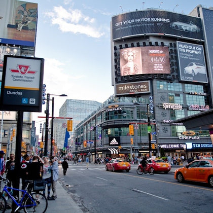 A busy urban intersection with pedestrians, vehicles, and large digital billboards displaying advertisements.