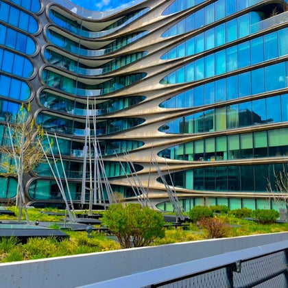 A modern building with curved geometric architecture, large glass windows, and landscaped greenery in the foreground.