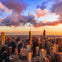 A city skyline at sunset with tall buildings and colorful clouds in the sky.