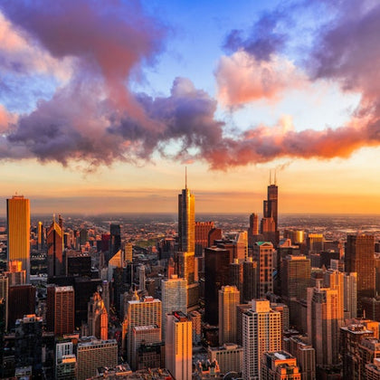 City skyline at sunset with tall buildings and colorful clouds in the sky.