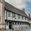 A historic black-and-white timber-framed building on a quiet street, with a hanging sign and a lamppost in front.
