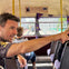 A man points out of a double-decker bus window, with passengers seated and a cityscape visible in the background.