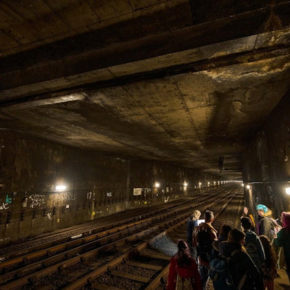 A group of people standing near the tracks inside a dimly lit underground subway tunnel.