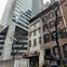 A street-level view of a modern high-rise next to older townhouses, one of which has a canopy labeled "Bill's."