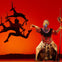 A theatrical performance featuring an actor in elaborate costume and makeup gesturing toward a silhouette of antelopes on stage.