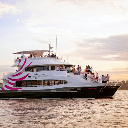A passenger boat with people on the deck, featuring pink stripes, cruising in calm waters at sunset.