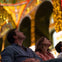 Two people seated indoors, looking upward with interest, surrounded by ornate, colorful architecture.