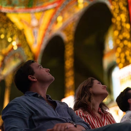 Two people seated indoors, looking upward with interest, surrounded by ornate, colorful architecture.