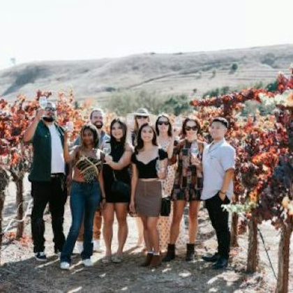 Three people smiling and posing in front of a sign that reads, "Welcome to this world famous wine growing region."