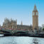 View of the Palace of Westminster and Big Ben near the Thames River, with red double-decker buses crossing a bridge.