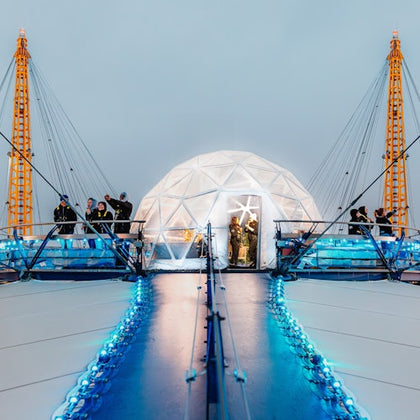 People gather on a modern rooftop platform with blue lights and a white geodesic dome, surrounded by yellow support structures.