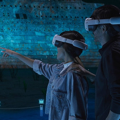 Two people wearing VR headsets interacting with an underwater scene, featuring a large sunken ship in the background.