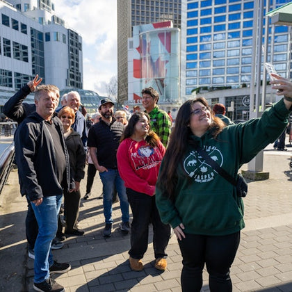 A group of people posing for a selfie outdoors in an urban area with modern buildings in the background.