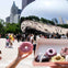 Person holding a pink doughnut with a box of assorted doughnuts in front of the reflective Cloud Gate sculpture in a busy plaza.