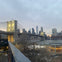 The Brooklyn Bridge at dusk, with city skyscrapers in the background and a park area in the foreground.