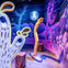 A colorful, surreal room with cartoonish cactus sculptures, a moon face on the wall, and vibrant painted backgrounds.