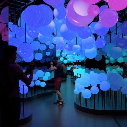 People walking through an illuminated art installation with glowing, multicolored orbs suspended on stands.