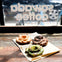 Three assorted crullers on a napkin, placed on a wooden surface in front of a window with "Swaggy Coffee USA" written on it.