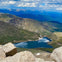 A scenic view of a mountain landscape with a clear lake below, surrounded by rocky terrain and distant mountain ranges.