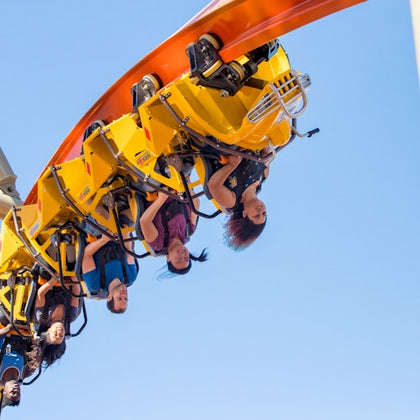 People riding a bright yellow roller coaster upside down on a loop under a clear blue sky.