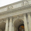 Facade of the New York Public Library with columns, arches, and statues under a cloudy sky.